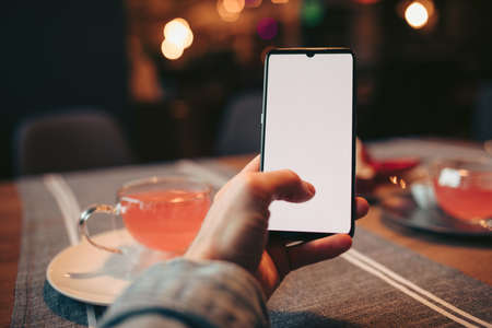 Male hand holding smartphone with blank display and finger on screen in cafeの写真素材