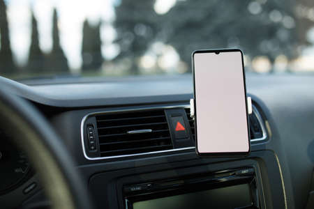 Smartphone with blank white display in a car phone holder, mockup