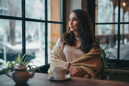 Portrait of beautiful woman dreaming looking through window in cafeの写真素材