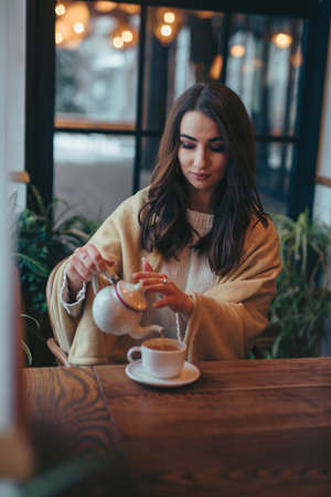 Woman pouring tea into the cup in cafeの写真素材