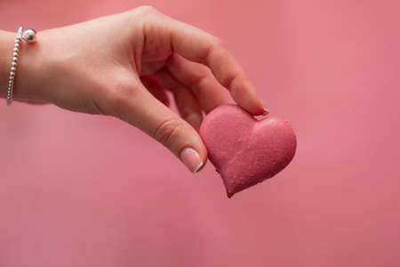 Female hand holding pink macaroon in the heart shapeの写真素材