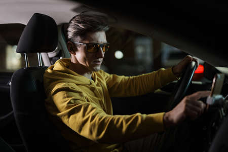 Driver man using smartphone in car phone holder at night