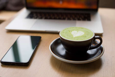 Workplace with matcha latte, cup with drink, laptop and smartphone on the tableの写真素材