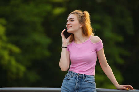 Smiling woman talk by phone in the park, green trees on background, communication conceptの写真素材