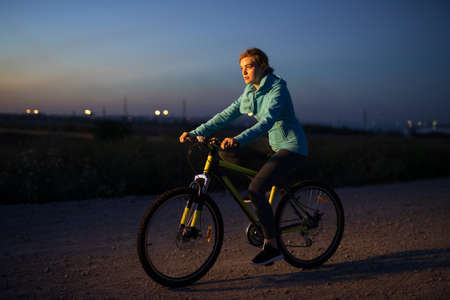 Young woman cycling on bicycle at countryside road at the nightの写真素材