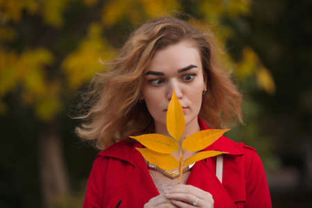 Portrait of woman in red coat holding yellow autumn leaf
