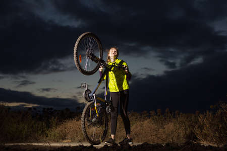 Sport woman with bicycle standing against dramatic sky backgroundの写真素材