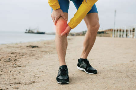 Runner man with knee injury and pain on the beachの写真素材