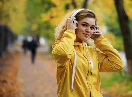 Woman in yellow jacket listens a music at the fall dayの写真素材