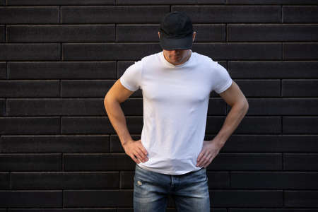 Mockup of man in empty white t-shirt standing against brick wallの写真素材
