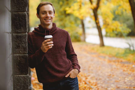 Man drinks a hot tea walking along alley at the fall day