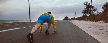 Unrecognizable runner man ready to run on the road from a low start, back view