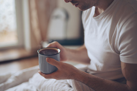 Man drinks hot tea at the morning sitting in a bedの写真素材
