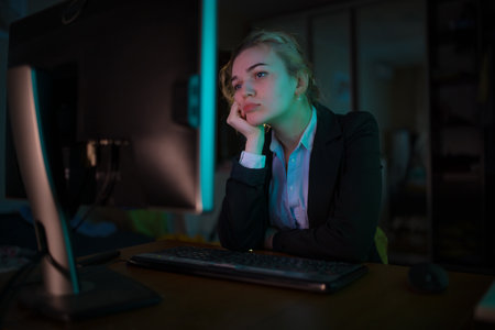 Young tired business woman office worker sitting near PC at late night leaning head on handの写真素材