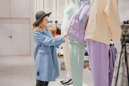 Woman chooses a jacket in the store while standing near the mannequins