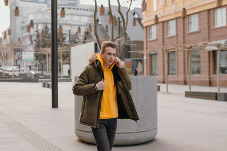 Handsome stylish man walks in a winter city with wireless earbuds in his ears