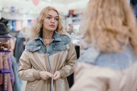 Young woman trying on a jacket in the store looking at herself in the mirrorの写真素材