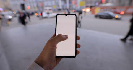 Male hand holding smartphone mockup in a city tap on a touchscreen empty screen chromakeyの写真素材