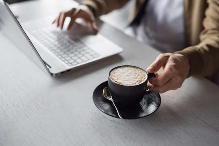 Closeup male hands working by laptop keyboard take a cup of latteの写真素材