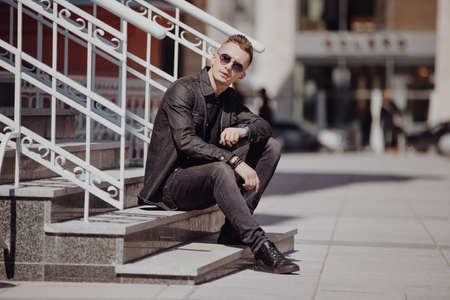 Young fashion man sitting in a city street wearing sunglassesの写真素材