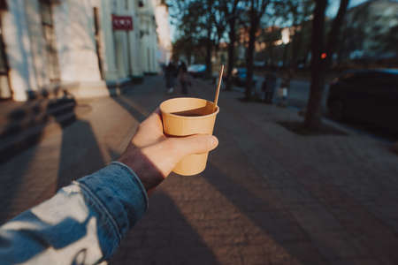 POV man holding cup with takeaway tea and lemon slice at the morning city