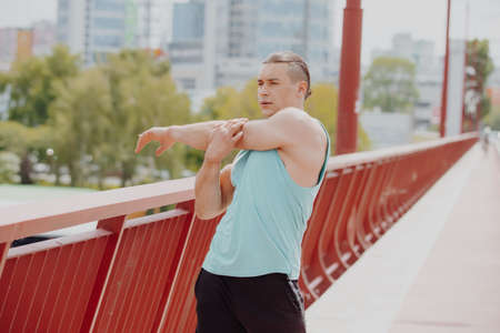 Athlete man stretches hands on a bridge in cityの写真素材