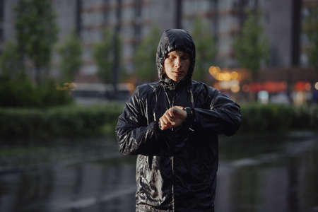 Man jogger looks a time on his watch under rain, flash lightの写真素材