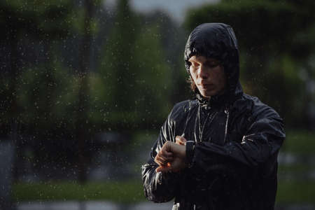 Man jogger looks a time on his watch under rain, flash lightの写真素材