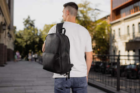 Rear view man walking in city with black leather backpack on his shouldersの写真素材