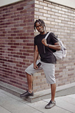 Fashion portrait of African man standing near brick wall with backpack