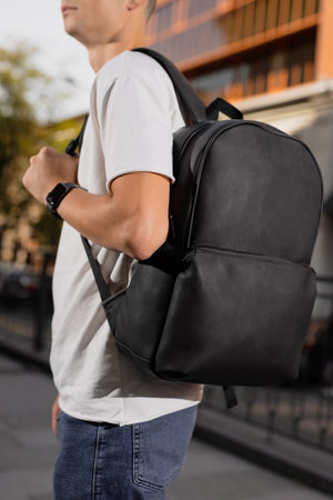 Rear view man walking in city with black leather backpack on his shouldersの写真素材