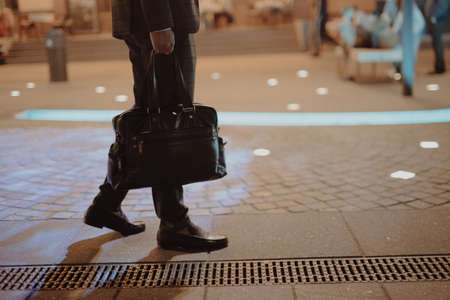 Man in classical suit walking with bag at night city on pavementの写真素材