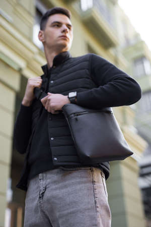 Man holding black leather messenger bag in a cityの写真素材