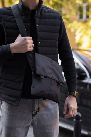 Closeup unrecognizable man holding black messenger bag in a cityの写真素材