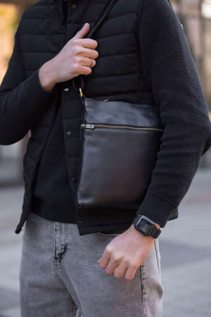 Closeup unrecognizable man holding black leather messenger bag in a cityの写真素材
