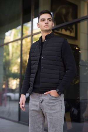 Fashionable man in black costume and vest posing in a cityの写真素材