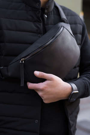 Closeup unrecognizable man holding black leather banana bag in a cityの写真素材