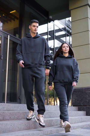 Stylish fashionable couple in black costumes going down the steps of the building