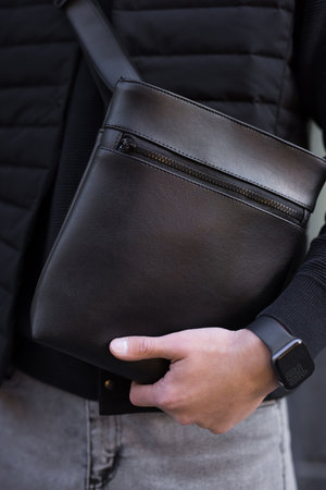 Closeup unrecognizable man holding black leather messenger bag in a cityの写真素材