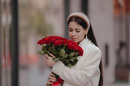 Happy woman carries and sniffs bouquet of flowers walking around the cityの写真素材