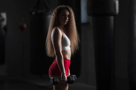 Fit woman portrait, standing with dumbbells in the gymの写真素材
