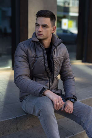 Man posing sitting in city wearing winter jacketの写真素材