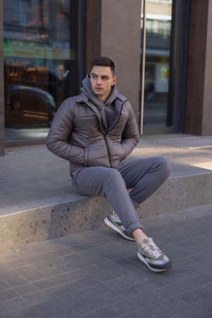 Man posing sitting in city wearing winter jacketの写真素材