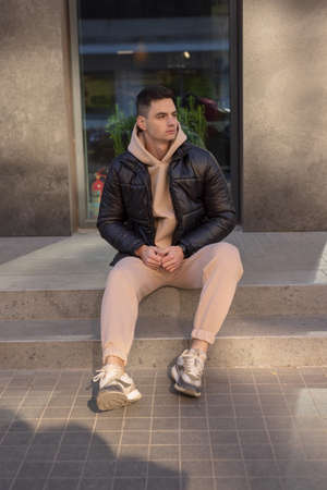 Man posing sitting in city wearing black winter jacketの写真素材