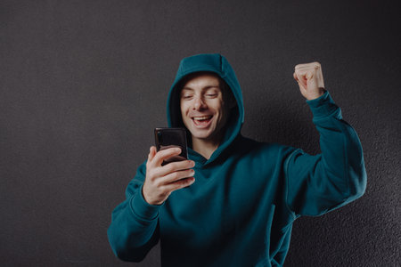 Happy lucky man in hoodie using smartphone win a jackpotの写真素材