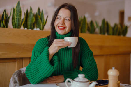 Smiling woman drinks coffee sitting at the table in cafeの写真素材