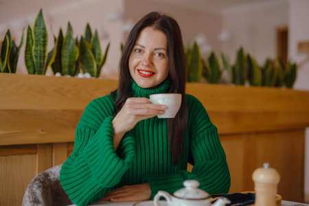 Smiling woman drinks coffee sitting at the table in cafeの写真素材