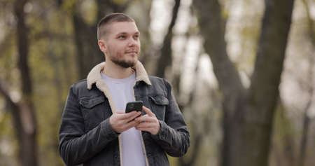 Smiling man use smartphone walking in the park at spring dayの写真素材