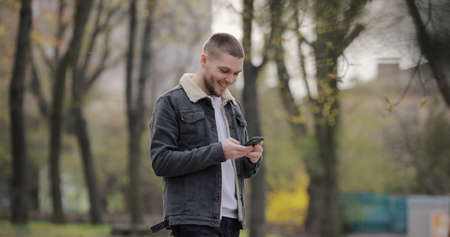 Smiling man use smartphone walking in the park at spring dayの写真素材