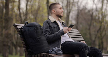 Man use smartphone sitting on bench in the park at spring dayの写真素材